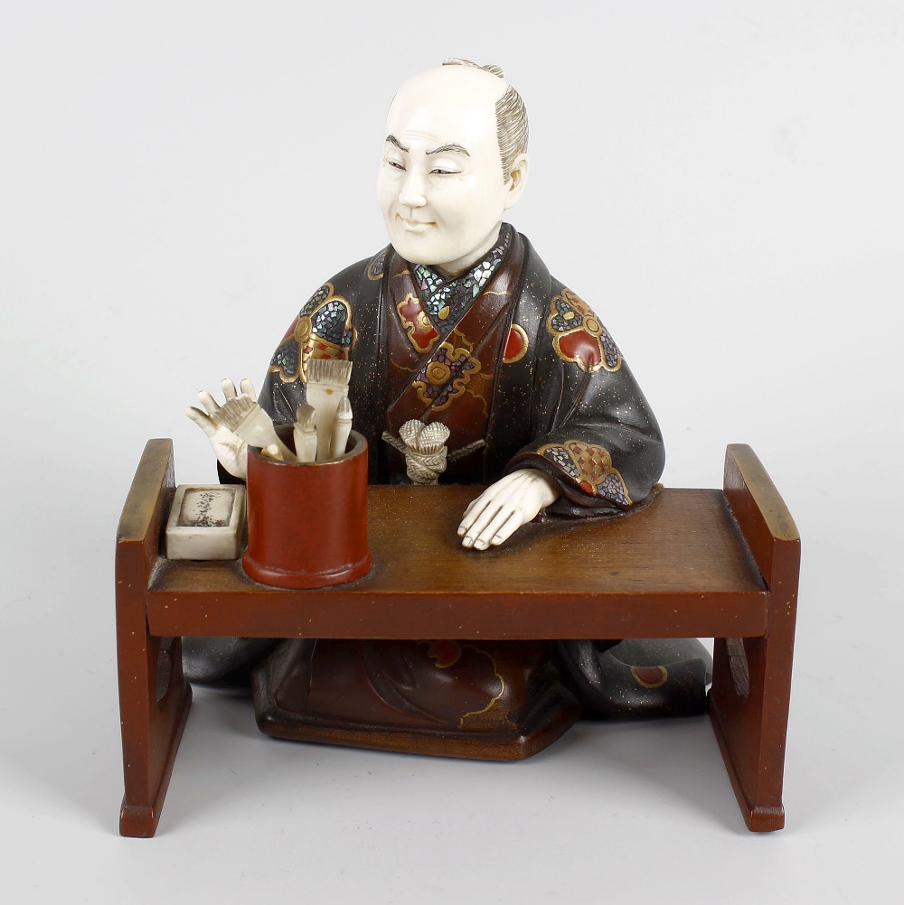 A Japanese Meiji period ivory and lacquer figure of a scholar knelt at a table, with right arm