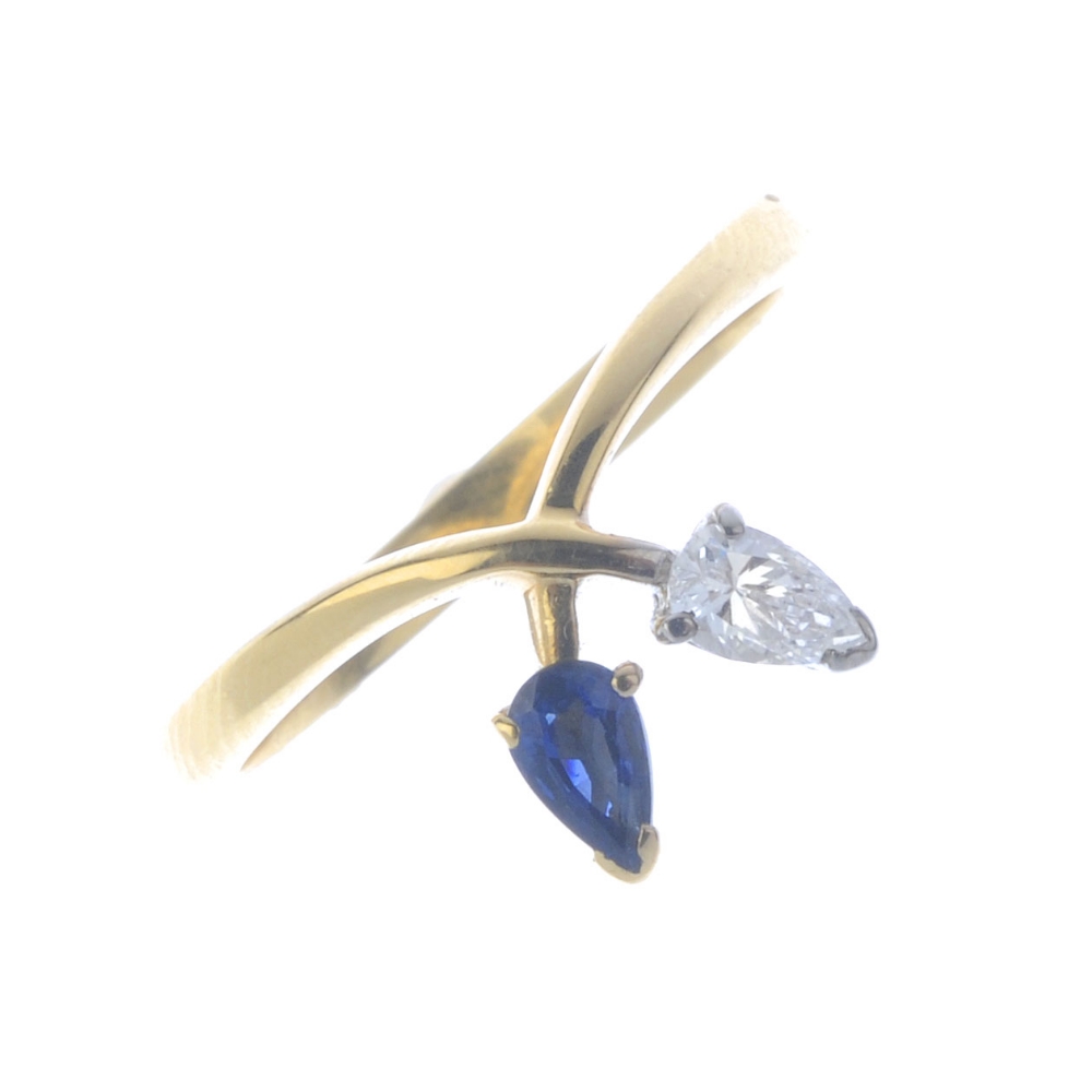 An 18ct gold diamond and sapphire dress ring. The crossover band, with pear-shape diamond and