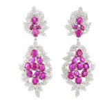 A pair of ruby and diamond earrings. Each of floral design, the oval-shape ruby stepped cluster,