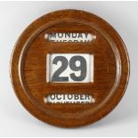 An early 20th century oak wall calendar, of circular form with three windows displaying day, date