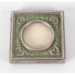 A small easel style white metal and green enamel panelled photograph frame, the glazed circular