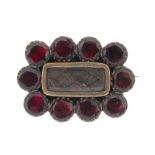 A mid Victorian garnet memorial brooch. The central glazed woven hair panel, with a surround of