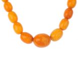 A natural amber bead necklace. Designed as a single row of fifty-two graduated oval-shape beads