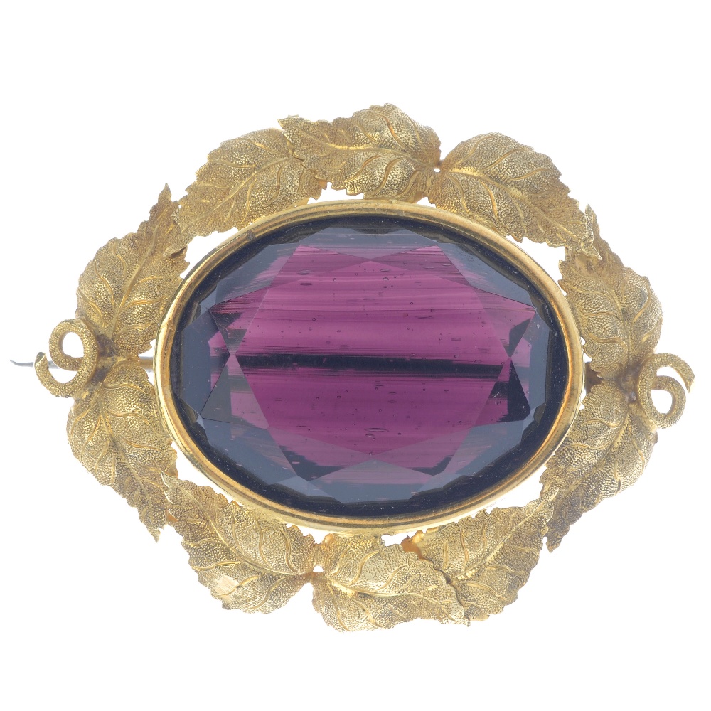 A late Victorian paste brooch. The oval-shape purple paste, within a textured foliate and vine