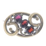 A late Victorian garnet three-stone brooch. The vari-shape garnet diagonal line, with scrolling