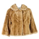 A light brown faux fur short jacket. Featuring a rounded collar, hook and eye fastenings and cropped