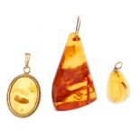 Three amber pendants. The first an oval modified amber cabochon, with rope-twist surround, the