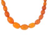 A natural amber bead necklace. The graduated single row of fifty-five oval-shape beads measuring 0.9