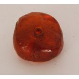 A fossilized circular amber bead with drilled hole to the centre with encased insect to interior,