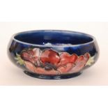 A Moorcroft footed bowl decorated in the Anemone pattern against a dark blue ground,