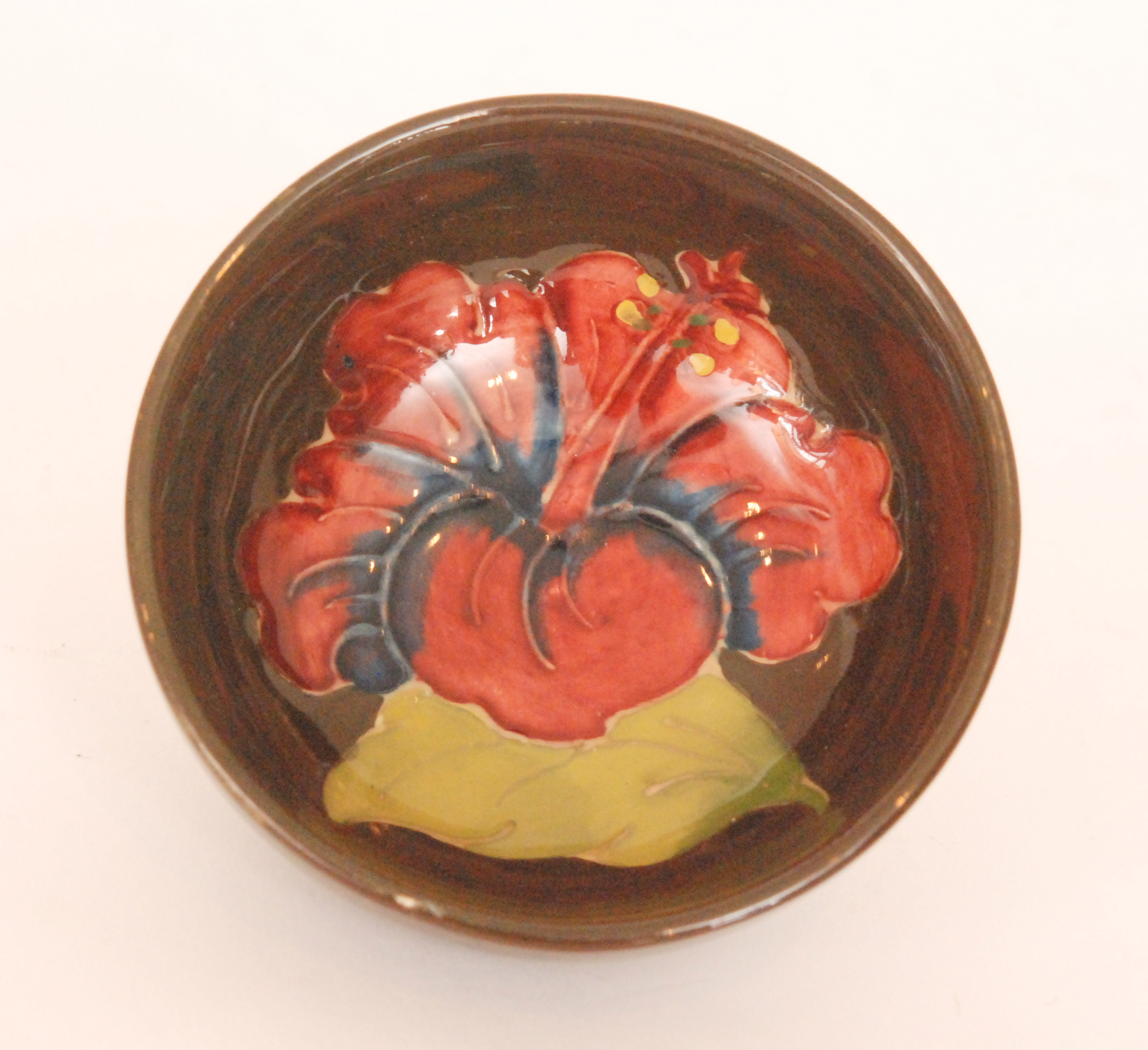 A Moorcroft footed circular bowl decorated in the Hibiscus pattern against a brown ground,