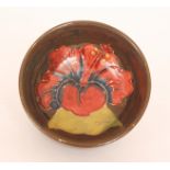 A Moorcroft footed circular bowl decorated in the Hibiscus pattern against a brown ground,