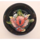 A Moorcroft footed bowl decorated in the Frilled Orchid pattern against a blue ground,