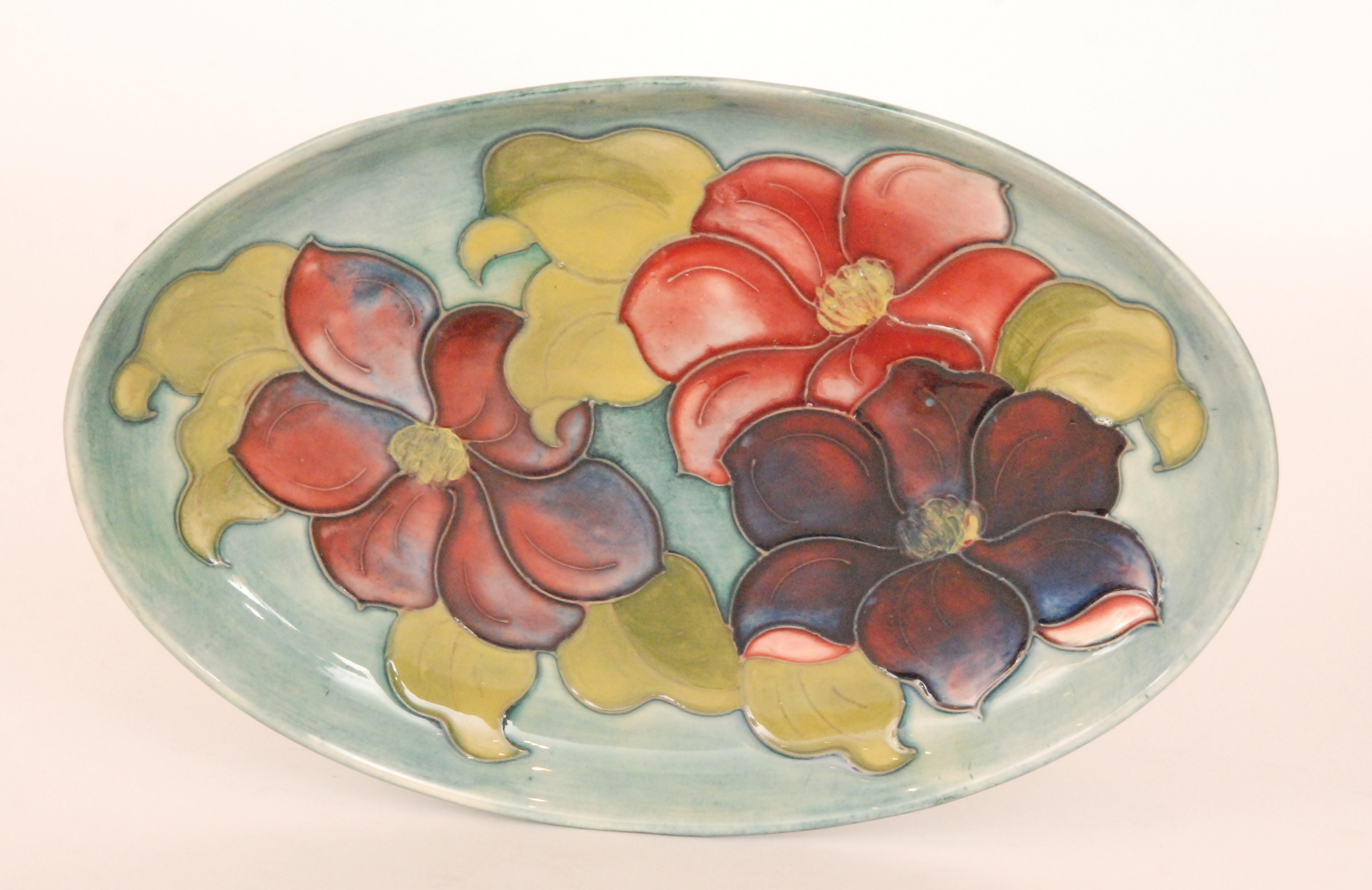 A Moorcroft shallow oval shaped dish decorated in the Clematis pattern against a blue green wash