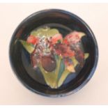 A Moorcroft footed circular bowl decorated in the Frilled Orchid pattern against a blue ground,