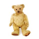 A small early 20th Century German blond plush teddy bear with brown glass eyes stitched paws and