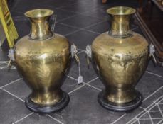 Pair Of Large Brass Vases, With Mask And Ring Handles, Raised On Circular Black Plinths,