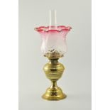 Brass oil lamp, ruby tinted and wrythen moulded shade, with chimney, height overall 49cm.