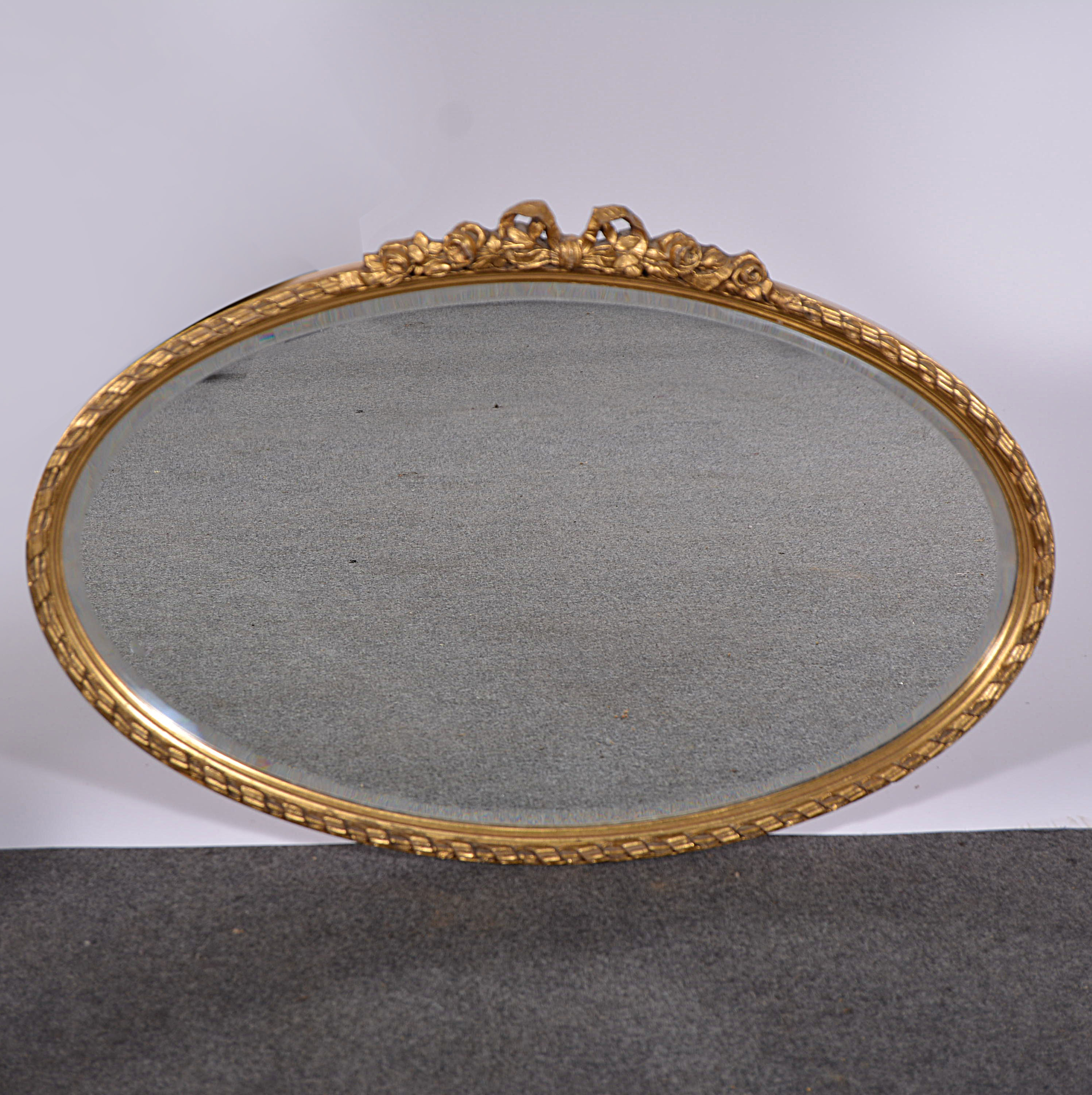 Oval wall mirror, gilded frame with flowers and ribbon ties above a plate, bevelled plate,