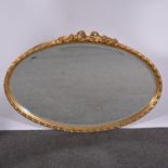 Oval wall mirror, gilded frame with flowers and ribbon ties above a plate, bevelled plate,