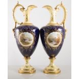 Pair of Coalport pedestal jugs, blue and yellow ground with painted reserves by E O Ball,