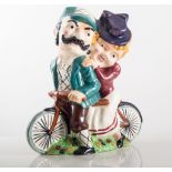 Shorter pottery lamp base, designed with a lady and gentleman riding a tandem, painted in colours,