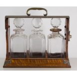 A three bottle oak tantalus with hinged brass top holding three plain glass decanters with faceted