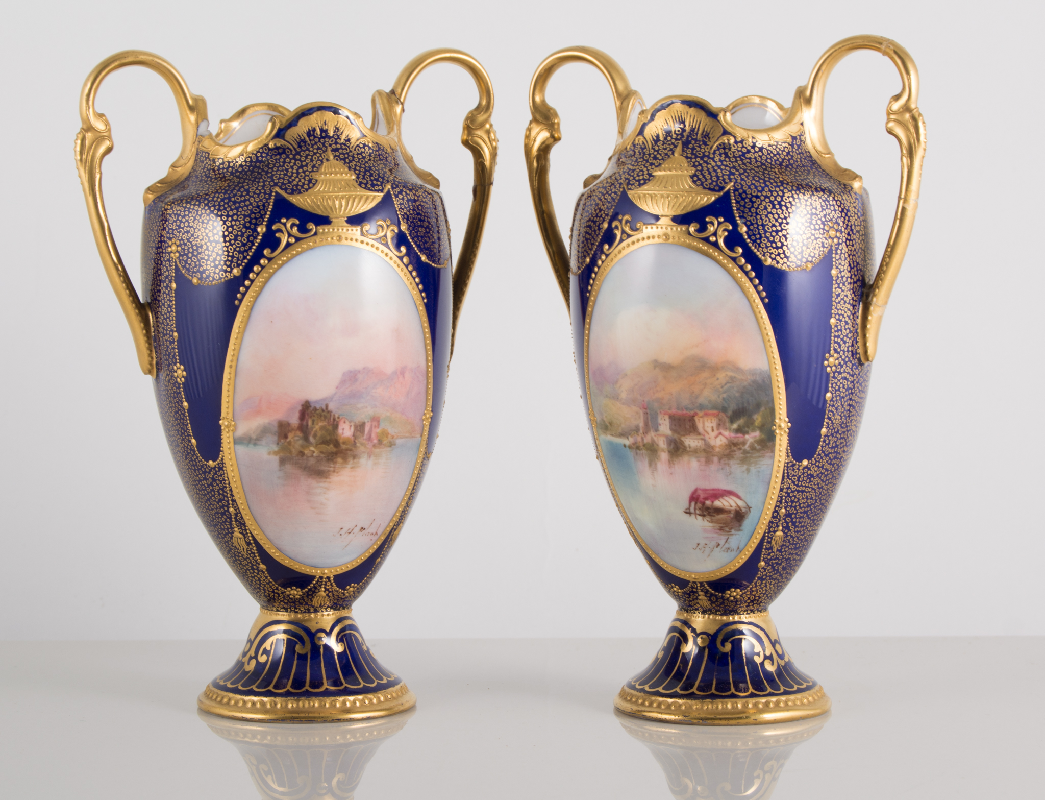 Pair of Royal Doulton cabinet vases, (both have repaired handles), painted with landscapes,