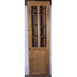 Narrow stripped pine bookcase, glazed panelled door to the upper section, panelled door below,