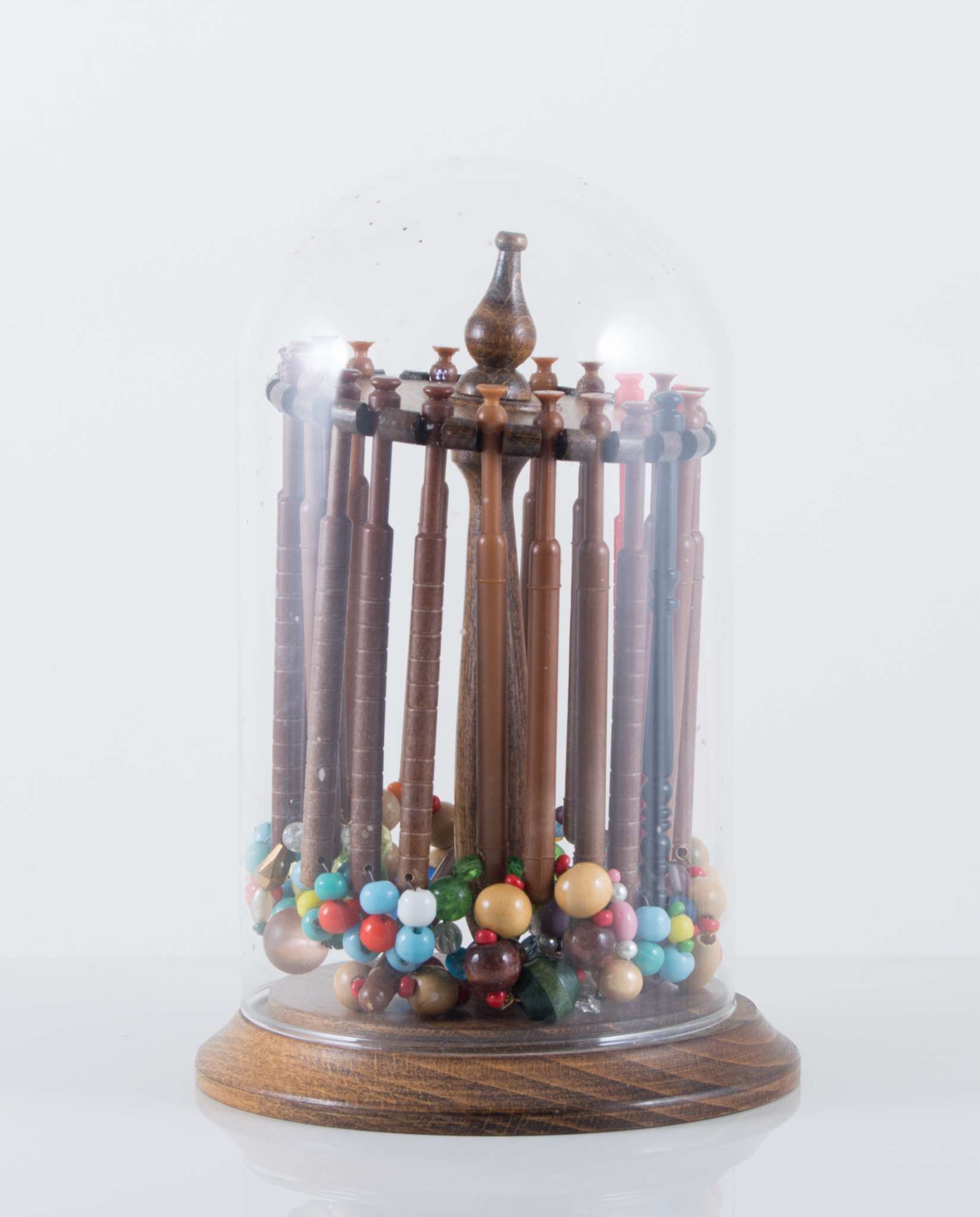 A glass dome 20cm, containing plastic pillow lace bobbins.