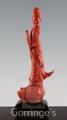 A large Chinese coral figure of Guanyin, holding a vase and a scroll and standing on a lotus