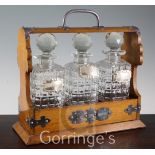 An Edwardian plated mounted oak three bottle tantalus, with three later silver spirit labels, Gin,