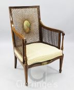 An Edwardian painted mahogany bergere armchair, with caned back and sides, and decorated with a