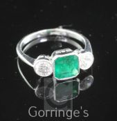 An 18ct white gold and three stone emerald and diamond ring, the central emerald weighing