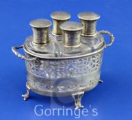 A George V pierced silver two handled scent bottle stand containing four silver mounted shaped glass