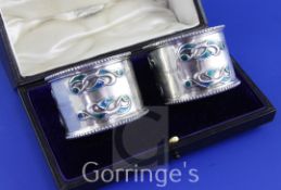 A cased pair of Edwardian Art Nouveau silver and enamel napkin rings by William Hair Haseler, with