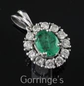 A white gold, emerald and diamond cluster pendant, of oval form, with oval cut emerald and round cut