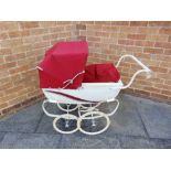 A SILVER CROSS DOLL'S PRAM the cream metal body with red side flashes, a red folding hood and apron,