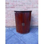 A FIGURED MAHOGANY BOW FRONT HANGING CORNER CUPBOARD with dentil frieze, 68cm wide 100cm high