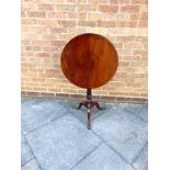 A GEORGIAN MAHOGANY OCCASIONAL TABLE the circular tilt-top raised on turned pedestal and on three