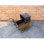 A DOLL'S PRAM circa 1920s, the lined olive green wooden body with a black rexine folding hood and