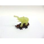 A CARVED JADE FIGURE OF AN ELEPHANT, standing with trunk raised, on hardwood stand 10cm high