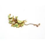 AN ENAMELLED PEARL SET HOLLY BROOCH stamped '18' to the pin, the realistic curled leaf with three