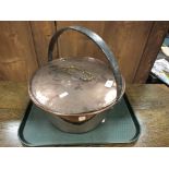 A copper jam pan and flat cover containing horse brasses.