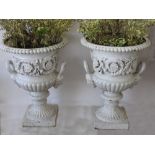 A pair and one single campana shaped cast iron garden urns with moulded edge over scrolling leaf
