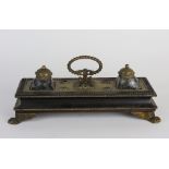 A 19th century Empire style ebonised and gilt metal ink stand with central loop handle and two ink
