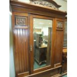 An Edwardian mahogany wardrobe with carved cresting above a bevelled mirror plate central door