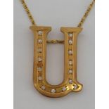 A yellow metal (tests as 14 carat gold) and diamond Alphabet pendant, designed as a 'U', 45mm long,