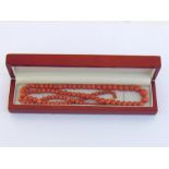 A coral bead necklace, composed of graduated spherical beads, on a cotton thread, to an ivory barrel