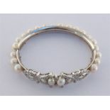 A rhodium plated gold (tests 14 carat), diamond and cultured pearl bangle, set along its length with